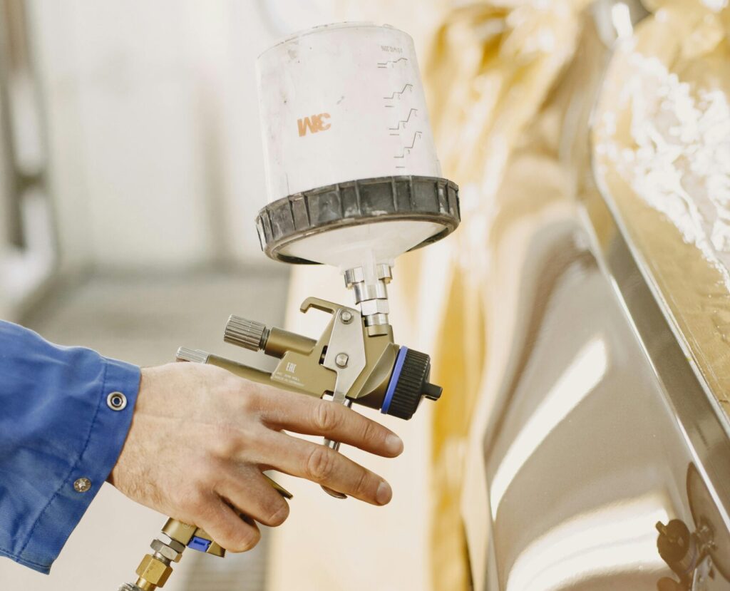 A technician spray paints a car with a paint spray gun in a workshop.